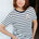 Woman wearing a black and white striped t-shirt with a small logo, standing against a plain background.