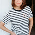 Woman wearing a black and white striped t-shirt with a small logo, standing against a plain background.