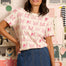 Woman wearing a white t-shirt with pink cat patterns in a room with posters and shelves.