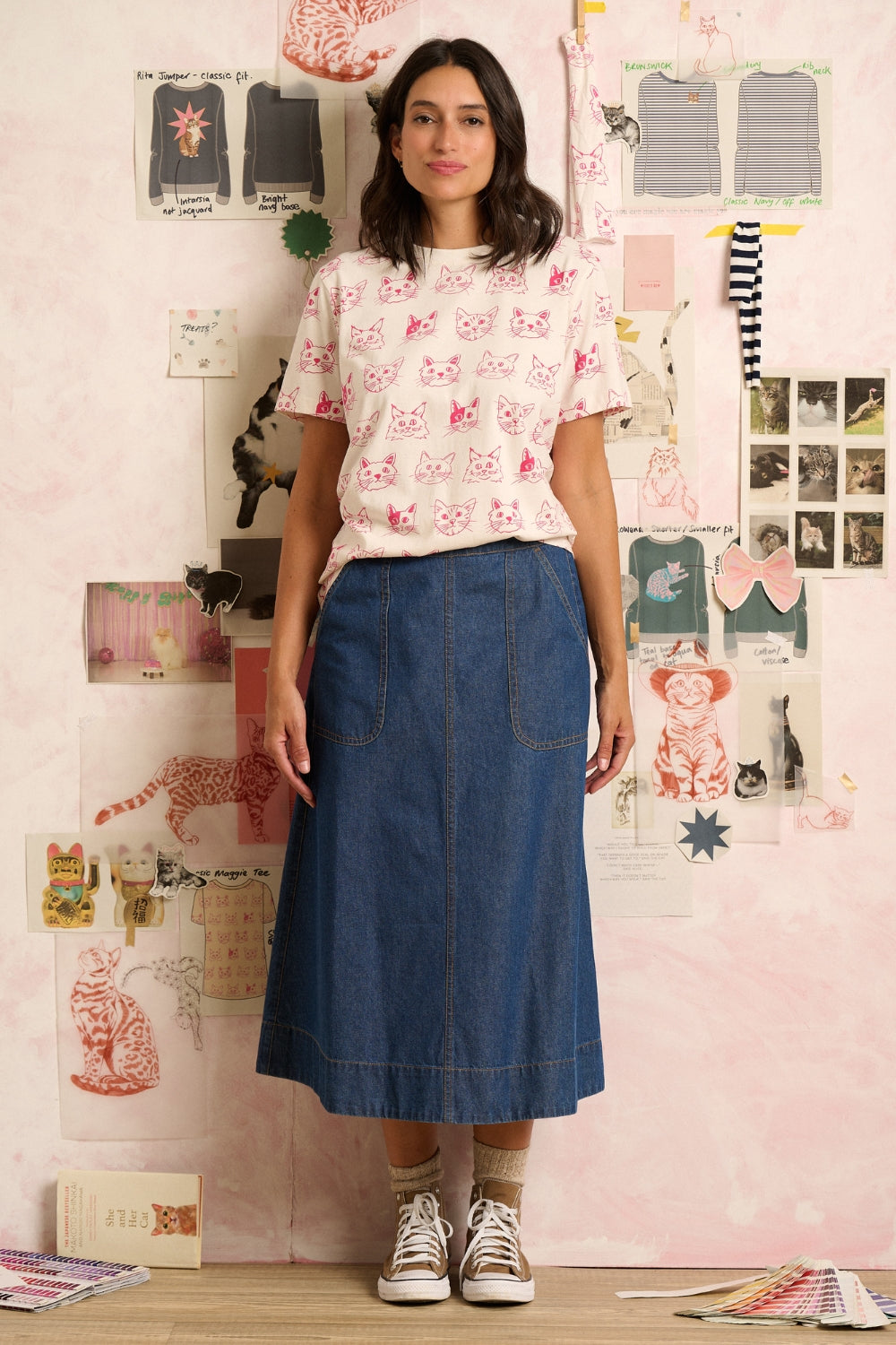 Woman wearing a white t-shirt with pink cat patterns in a room with posters and shelves.