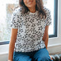 Woman wearing a white t-shirt with black star patterns sitting by a window.