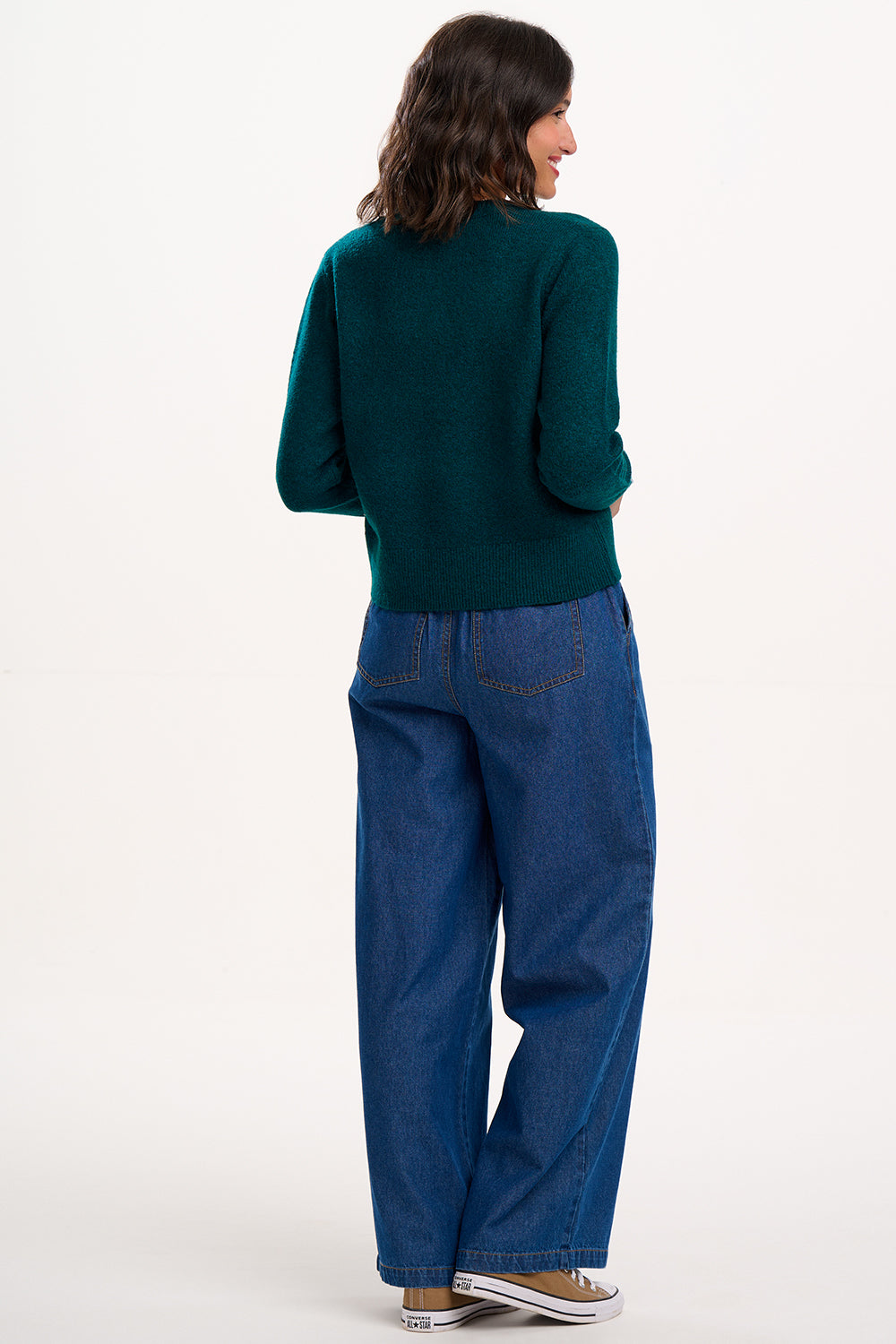 Woman wearing a teal sweater and blue jeans on a white background
