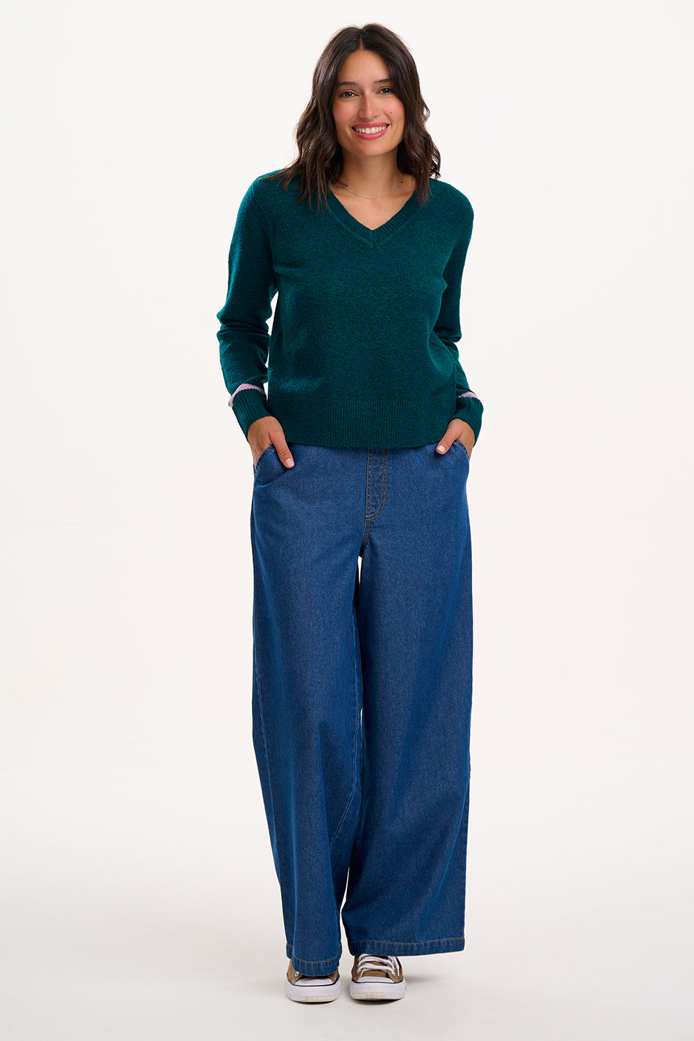 Woman wearing a teal sweater and blue pants on a white background