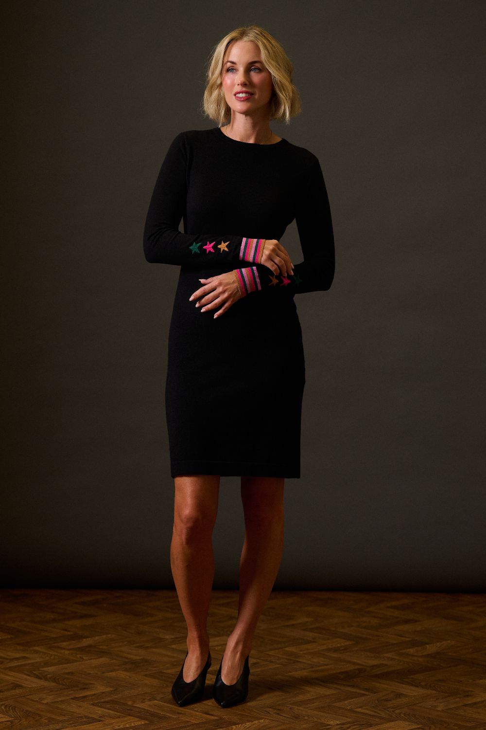 Woman wearing a black dress with colorful arm warmers against a dark background