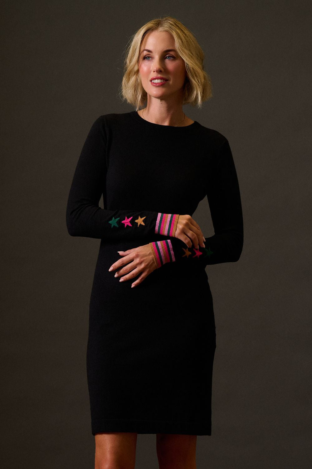 Woman wearing a black dress with colorful arm bands against a dark background