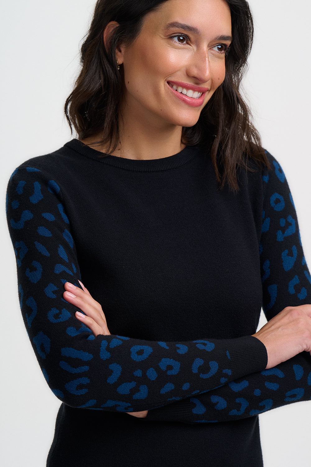 Woman wearing a black sweater with blue patterned sleeves against a white background