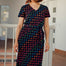 A model wearing a midi-length jersey dress with a V-neck, featuring a black base with a multicolored geometric wave pattern. The dress has a matching tie belt and short sleeves.