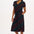 A model wearing a midi-length jersey dress with a V-neck, tie belt, and undulating multicoloured wave print. The dress is primarily black with red, pink, green, blue, and orange patterns.