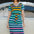 A person wearing a midi-length, V-neck, striped dress in green and multicolor, standing in front of a vintage car.