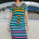 A person wearing a midi-length, V-neck, striped dress in green and multicolor, standing in front of a vintage car.