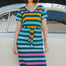 A person wearing a midi-length, V-neck, striped dress in green and multicolor, standing in front of a vintage car.