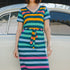 A person wearing a midi-length, V-neck, striped dress in green and multicolor, standing in front of a vintage car.