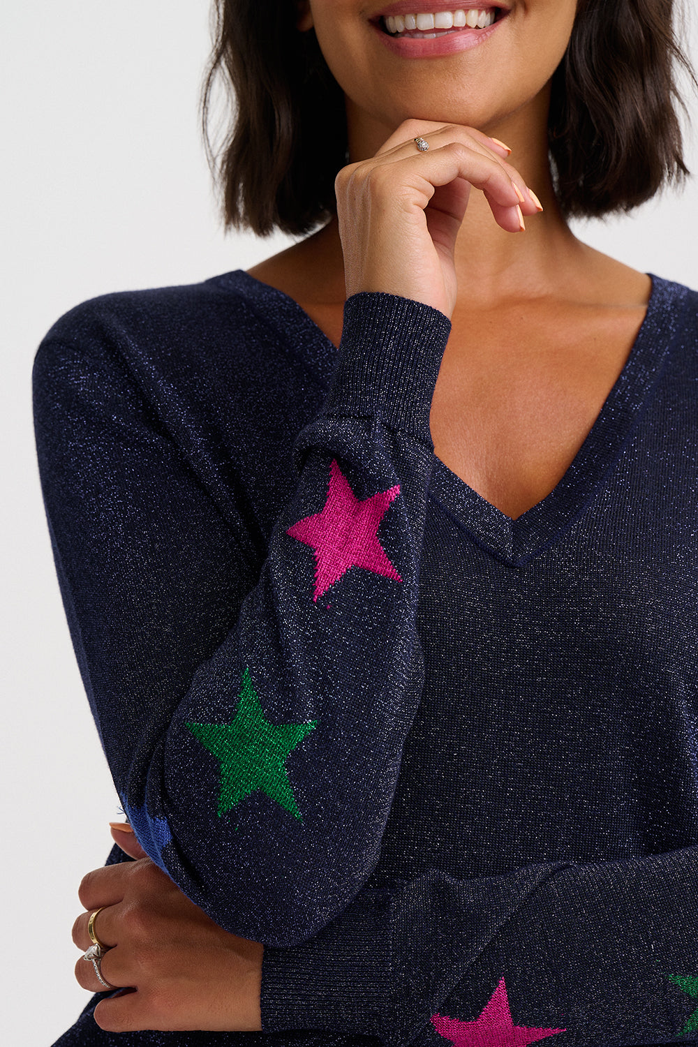 A close-up of a woman wearing a navy blue knit sweater with bright pink and green star patches on the sleeves, against a plain light gray background.