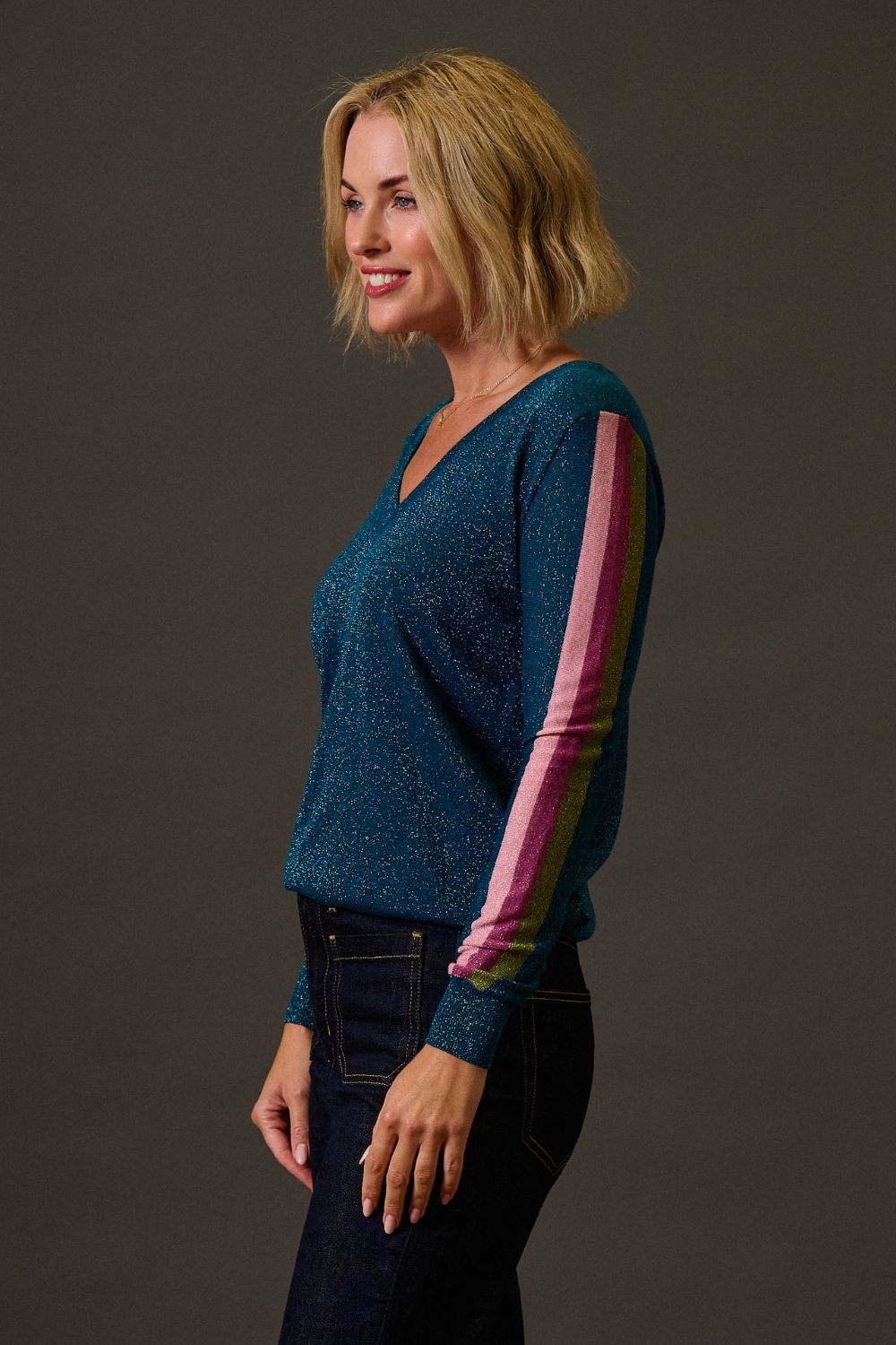 Woman wearing a blue sweater with colorful sleeves against a dark background