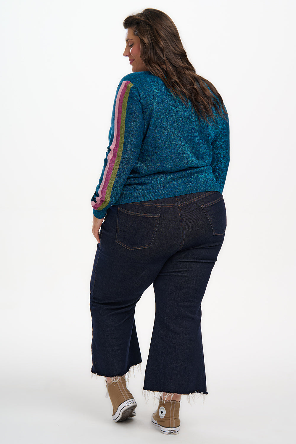 Person wearing a teal sweater with colorful stripes and dark blue jeans on a white background