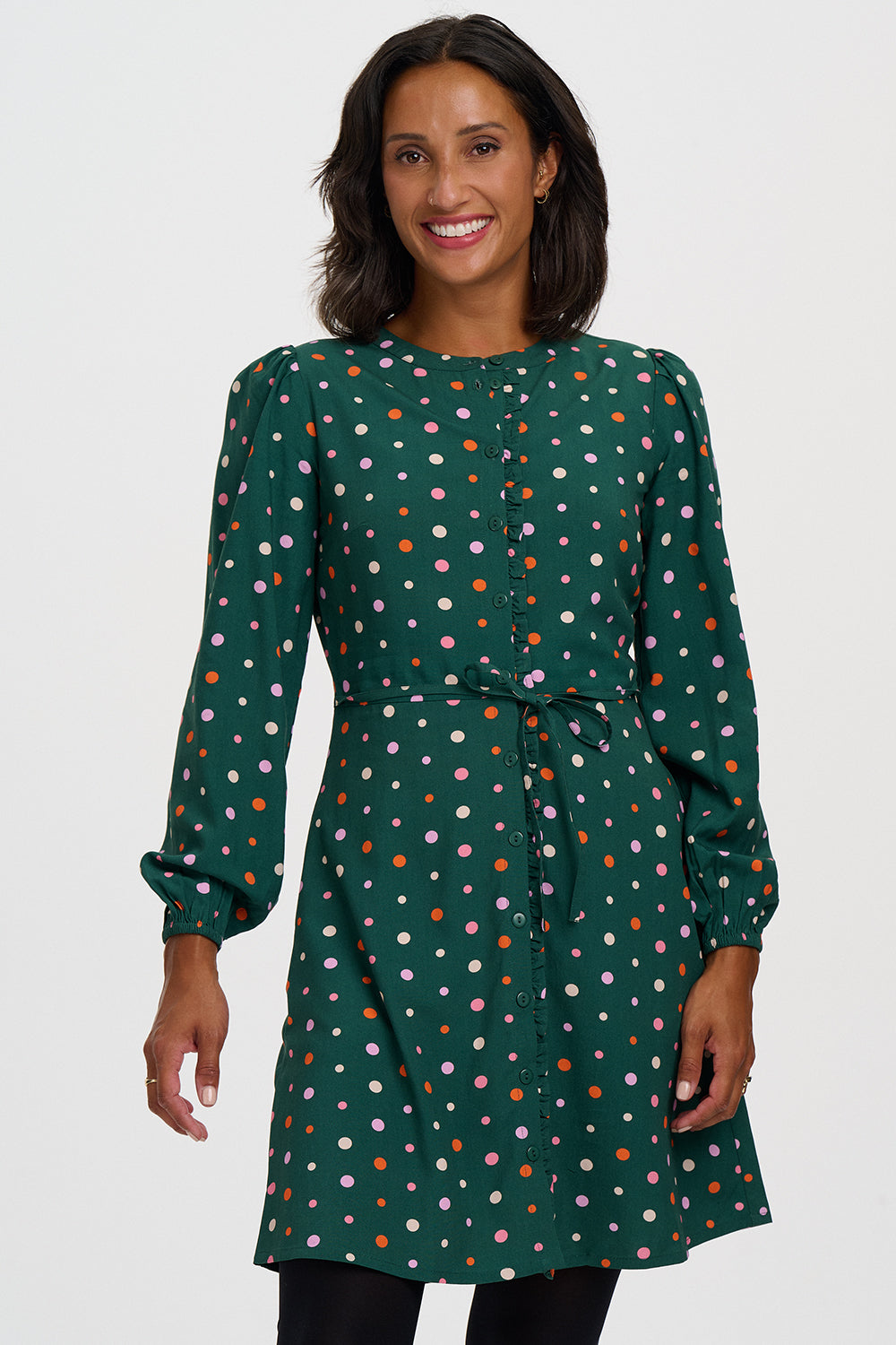 A woman wearing a dark green long-sleeve dress with a colorful polka dot pattern, featuring a tie waist and button-up front, set against a plain light gray background.