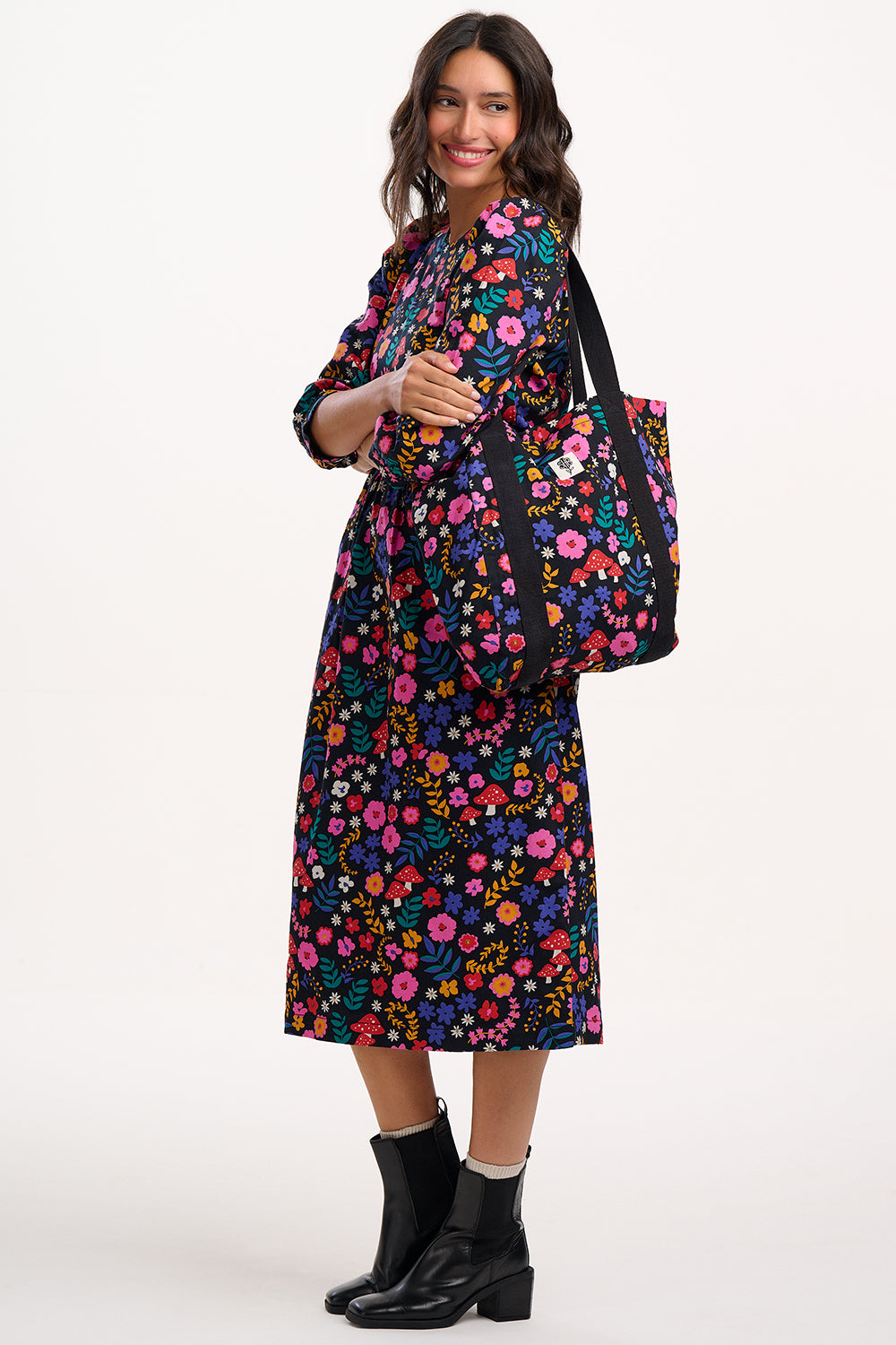 Woman wearing a floral dress holding a matching bag on a white background