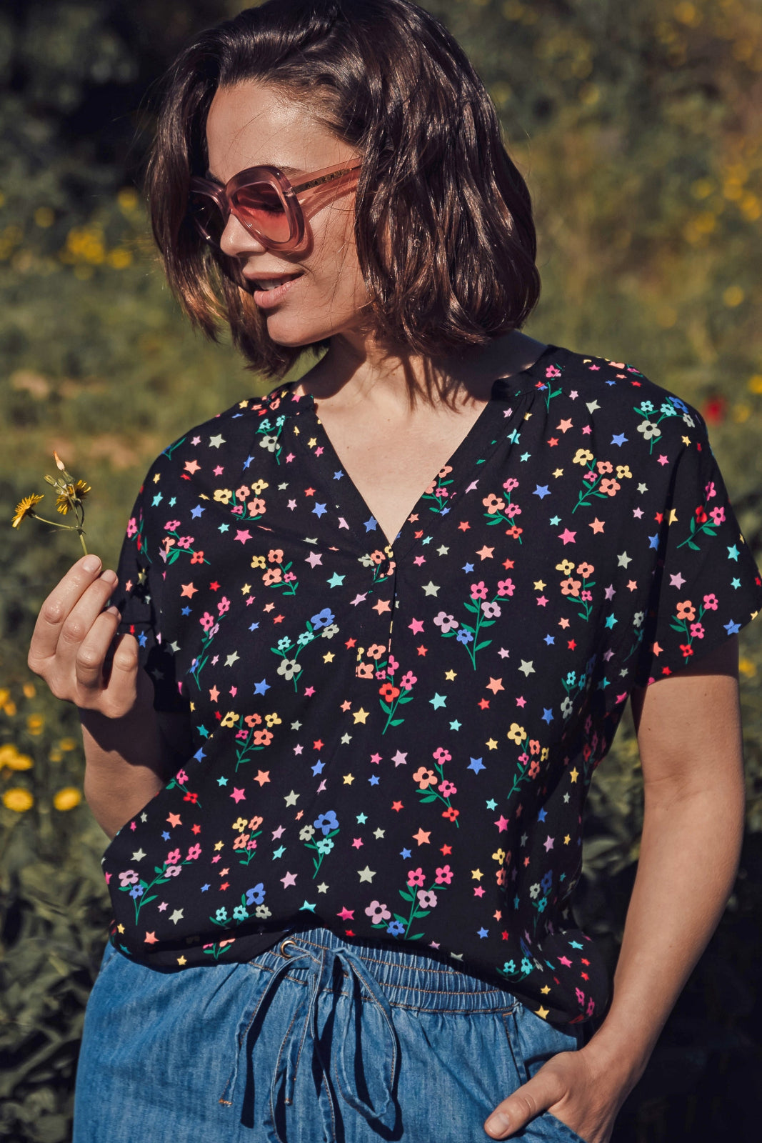 A woman wearing a black blouse with a multicolored floral and star print, round grandad collar, and cap sleeves.