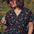 A woman wearing a black blouse with a multicolored floral and star print, round grandad collar, and cap sleeves.