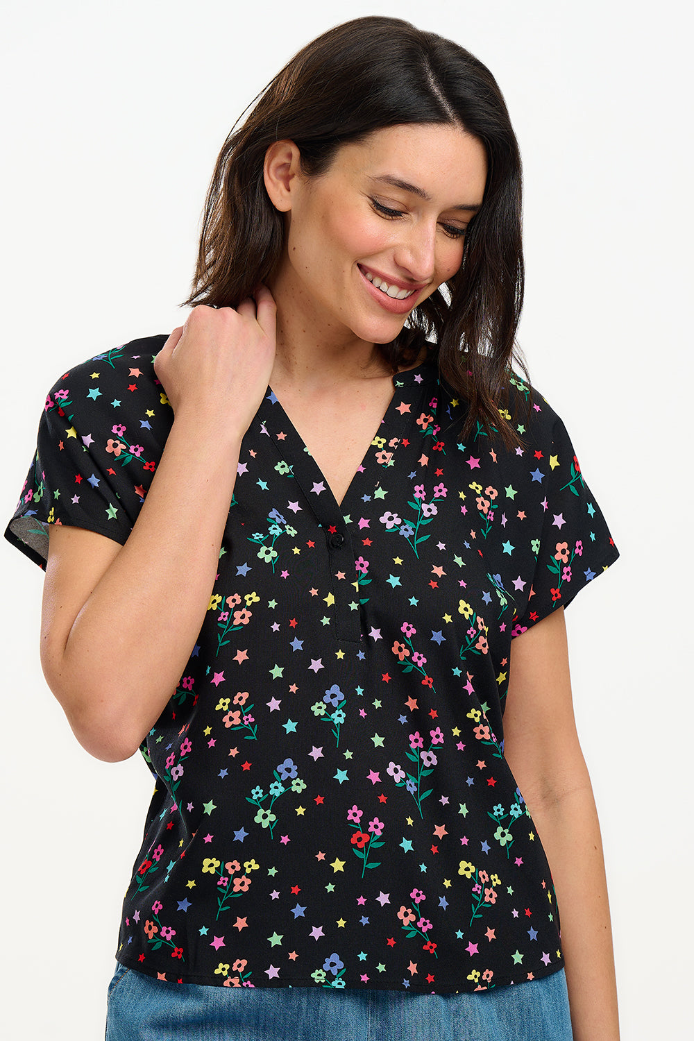 A woman smiling and wearing a black blouse with a colorful floral and star print, featuring a round grandad collar and short cap sleeves.