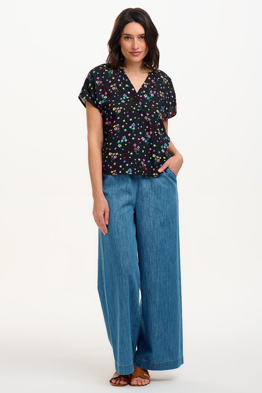 A woman smiling and wearing a black blouse with a colorful floral and star print, featuring a round grandad collar and short cap sleeves.