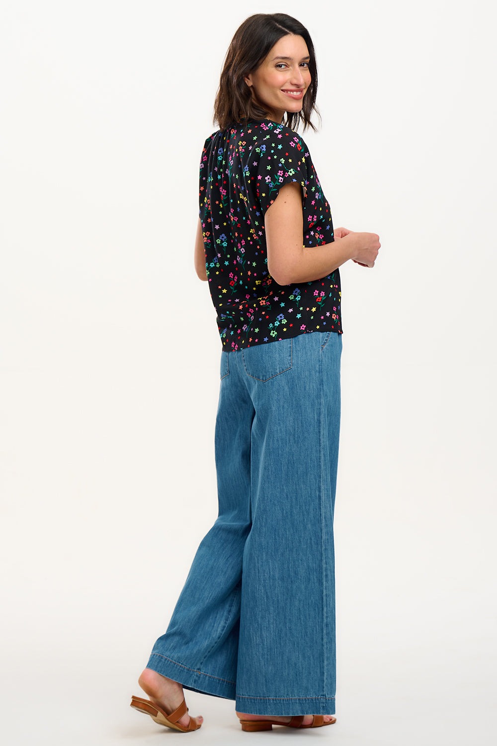 A woman smiling and wearing a black blouse with a colorful floral and star print, featuring a round grandad collar and short cap sleeves.
