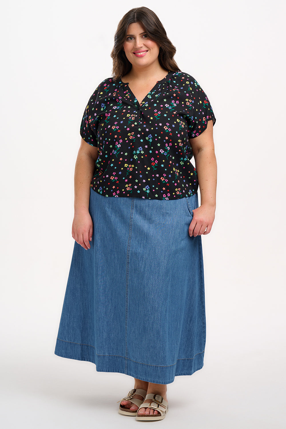 A woman smiling and wearing a black blouse with a colorful floral and star print, featuring a round grandad collar and short cap sleeves.