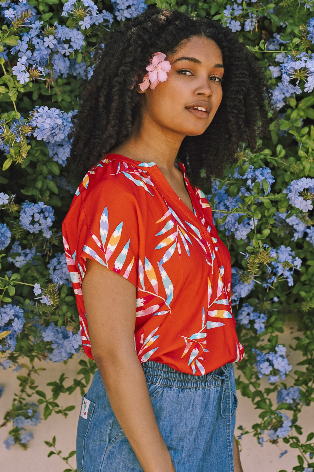 A woman wearing a red blouse with a vibrant Rainbow Fronds print, featuring colorful tropical leaves.