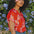 A woman wearing a red blouse with a vibrant Rainbow Fronds print, featuring colorful tropical leaves.