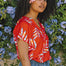 A woman wearing a red blouse with a vibrant Rainbow Fronds print, featuring colorful tropical leaves.