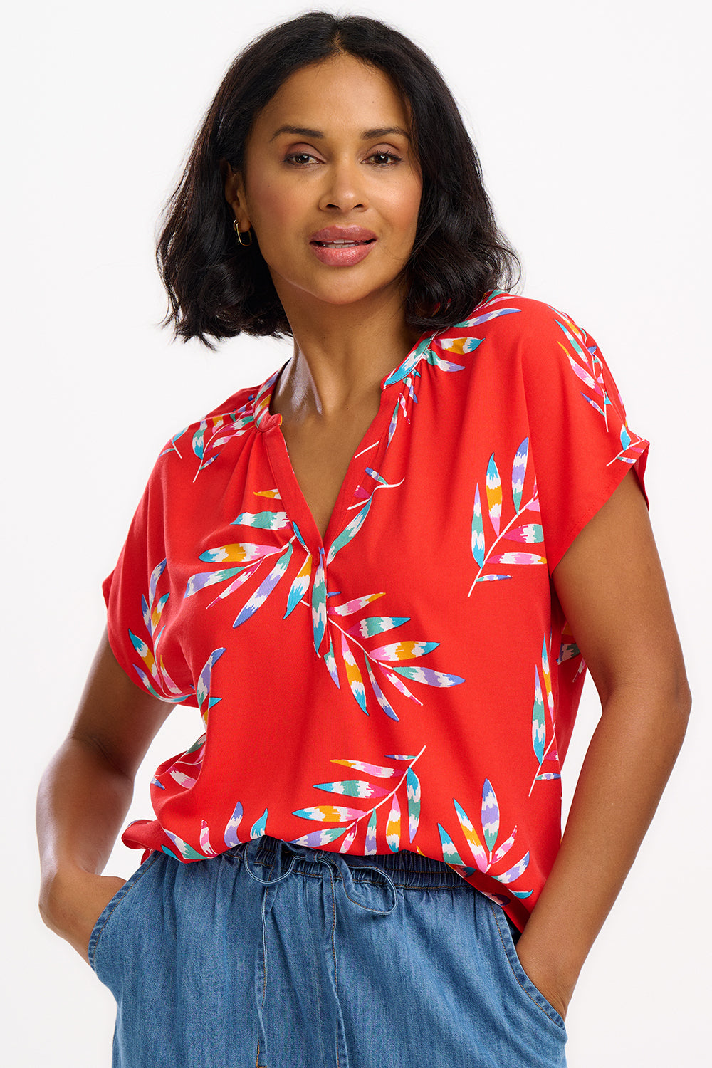 A woman modeling a red blouse with a tropical leaf print, featuring a round grandad collar and cap sleeves.