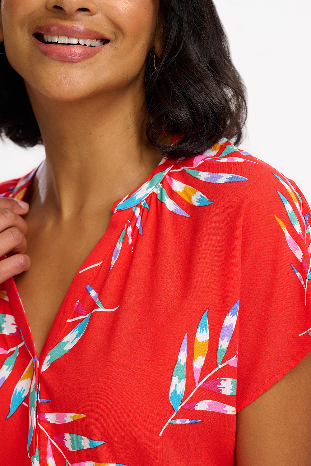 A woman modeling a red blouse with a tropical leaf print, featuring a round grandad collar and cap sleeves.