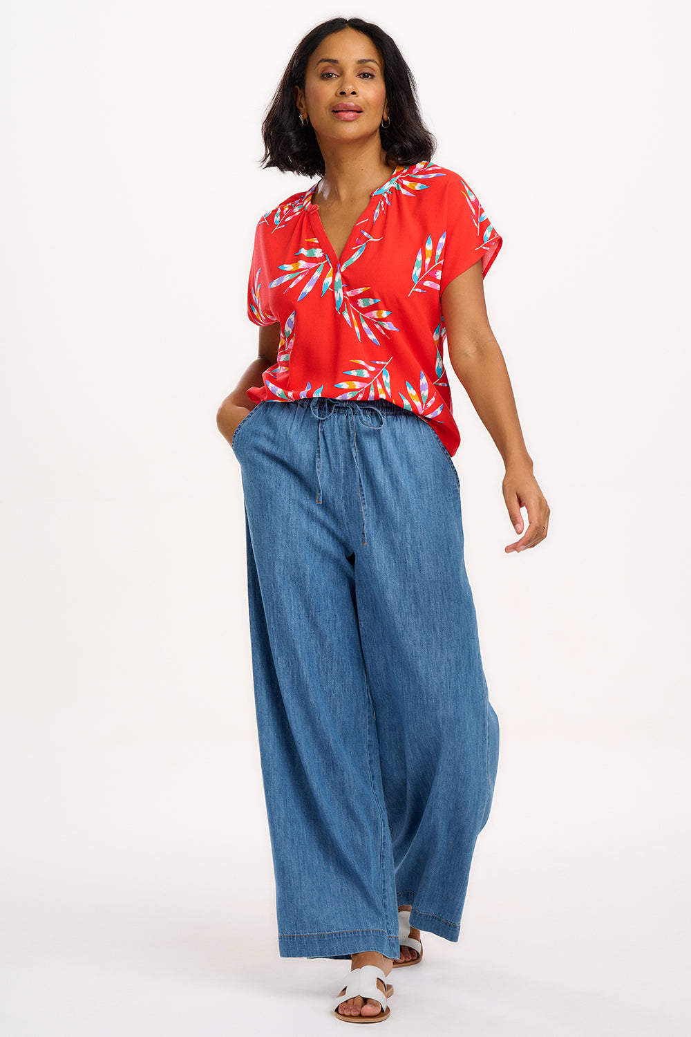 A woman modeling a red blouse with a tropical leaf print, featuring a round grandad collar and cap sleeves.