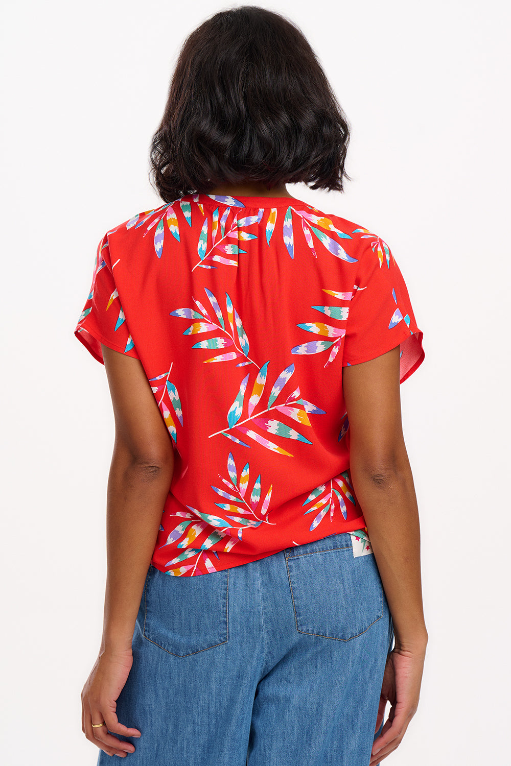 A woman modeling a red blouse with a tropical leaf print, featuring a round grandad collar and cap sleeves.