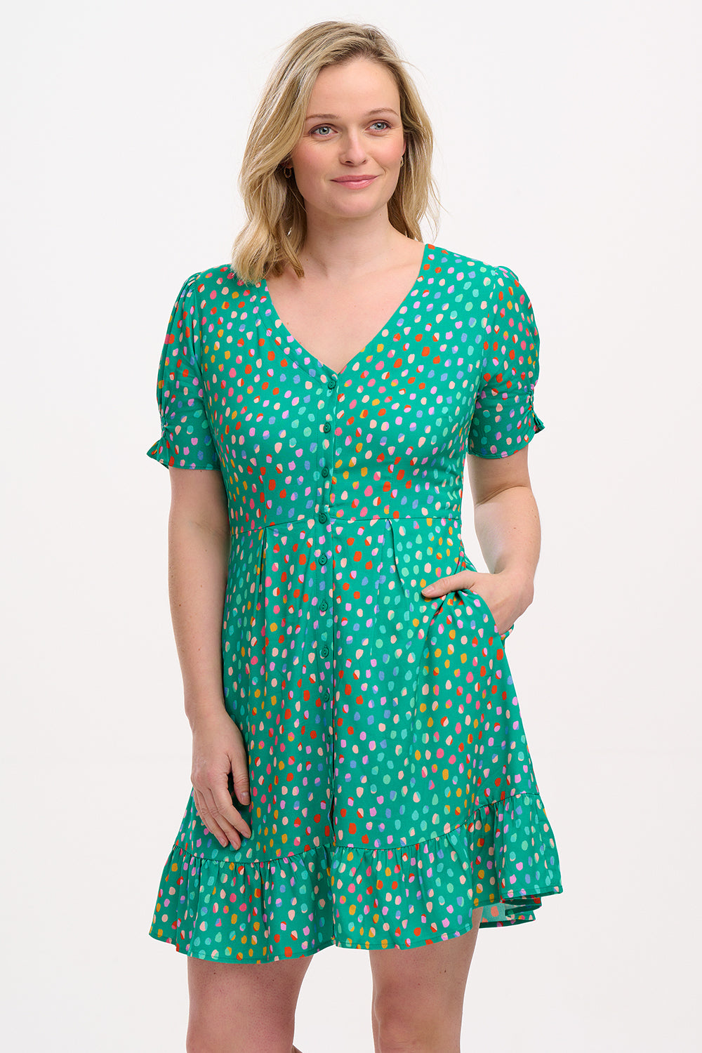 A woman wearing a green mini dress with a pattern of rainbow pebbles, featuring a V-neckline, puff sleeves, and a frill hem.