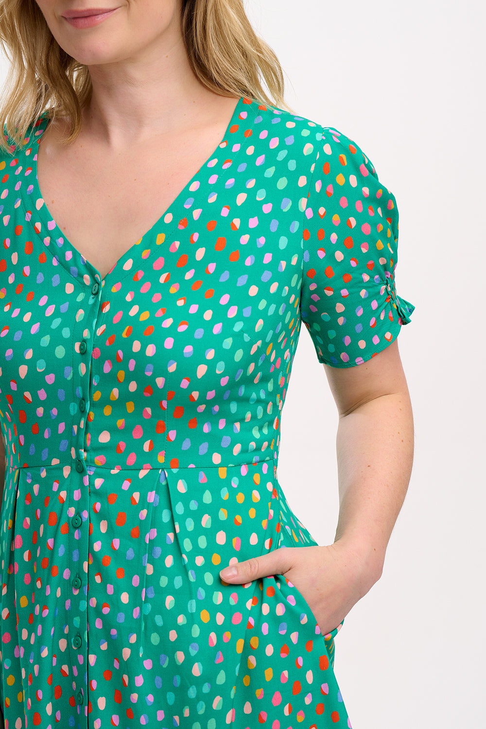 A woman wearing a green mini dress with a pattern of rainbow pebbles, featuring a V-neckline, puff sleeves, and a frill hem.