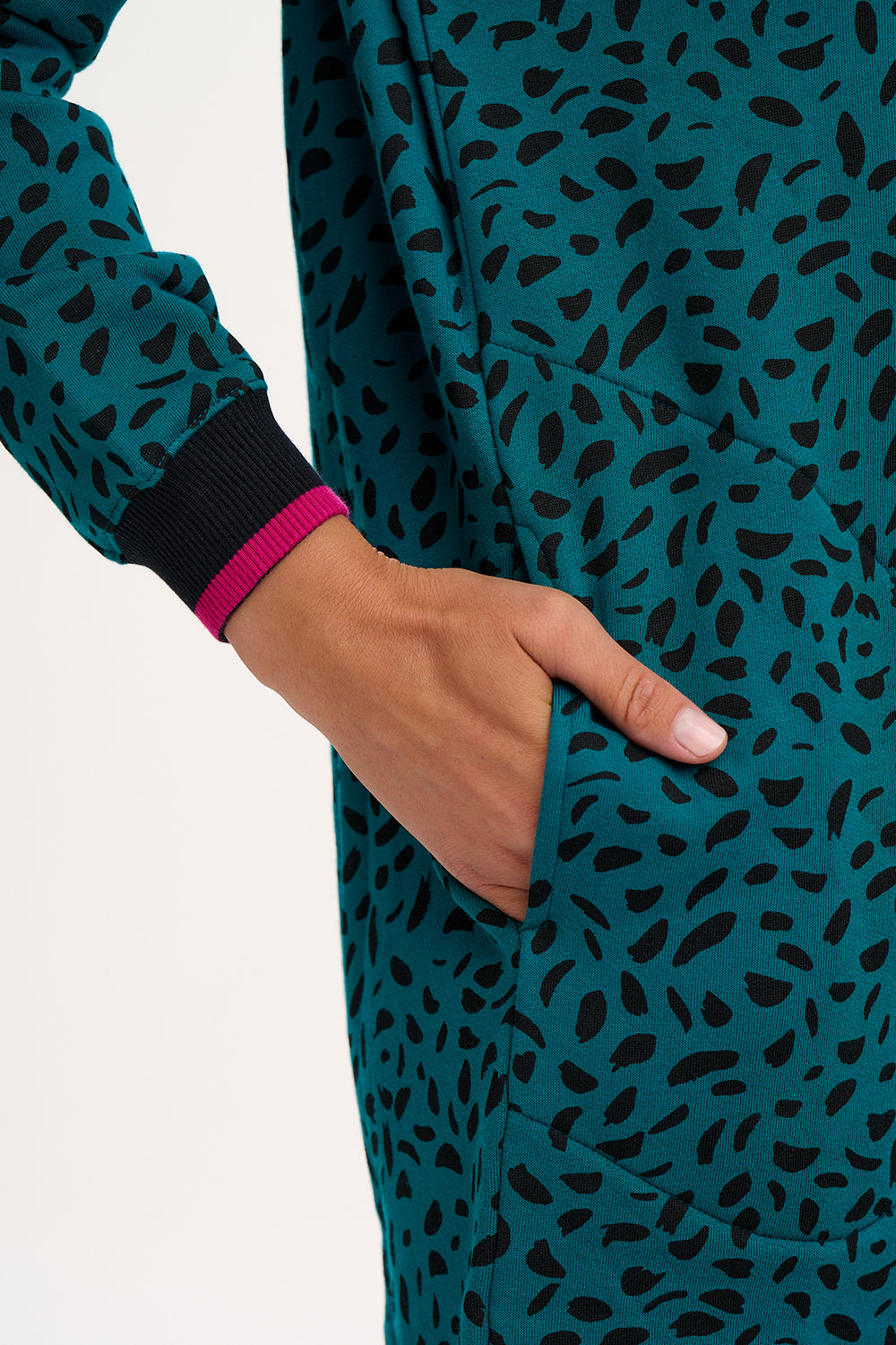 Close uop of teal outfit with black pattern and a hand in a pocket on a white background