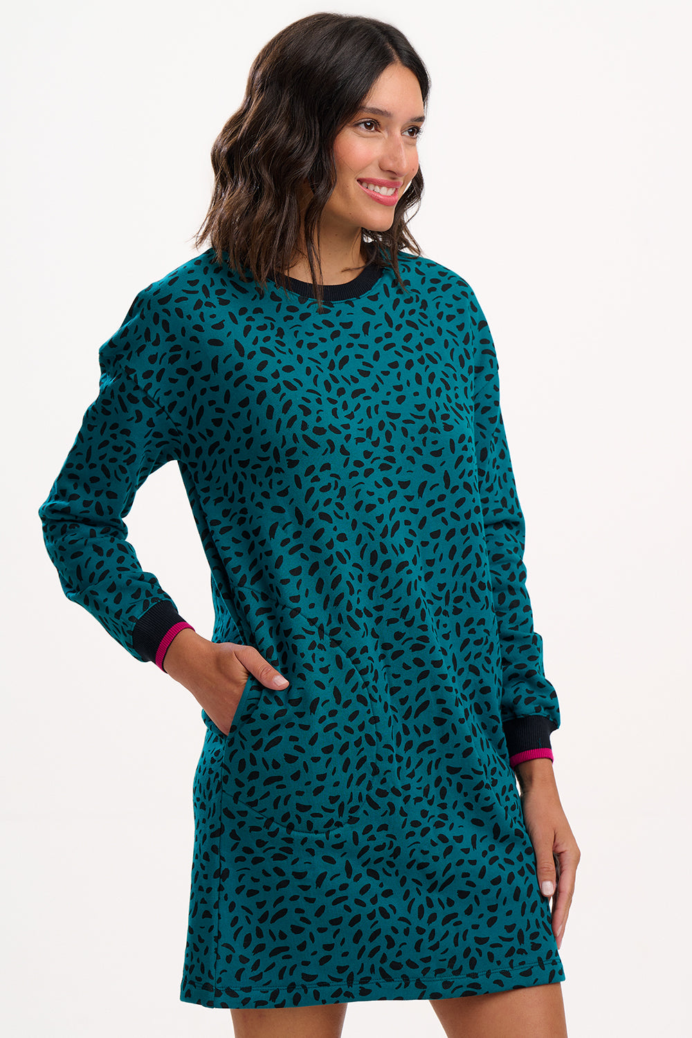 Sugarhill Brighton model wearing a teal patterned dress with black cuffs on a white background