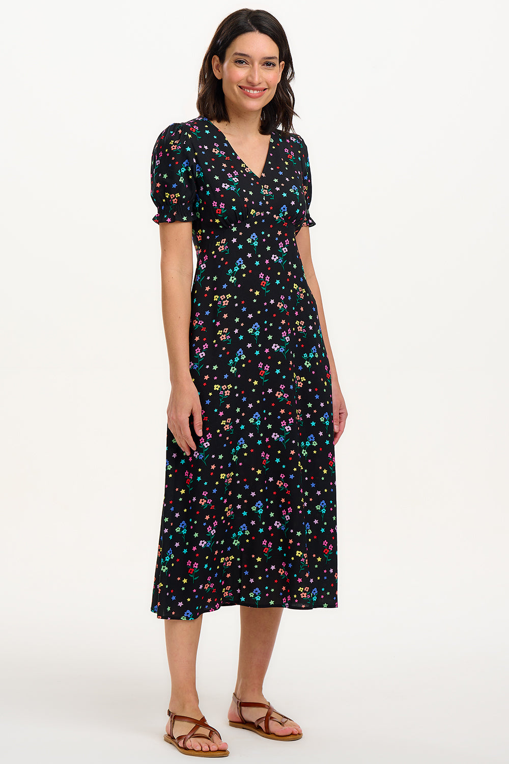A model wearing a mid-length black dress with a V-neck and short-shirred sleeves, adorned with a multicolor floral and star print.