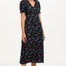 A model wearing a mid-length black dress with a V-neck and short-shirred sleeves, adorned with a multicolor floral and star print.