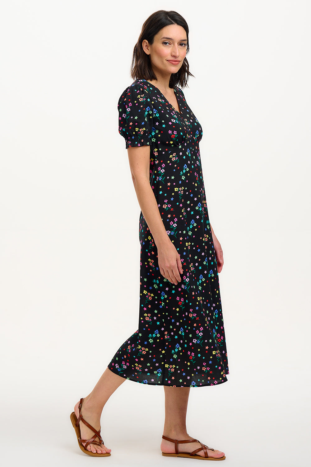 A model wearing a mid-length black dress with a V-neck and short-shirred sleeves, adorned with a multicolor floral and star print.