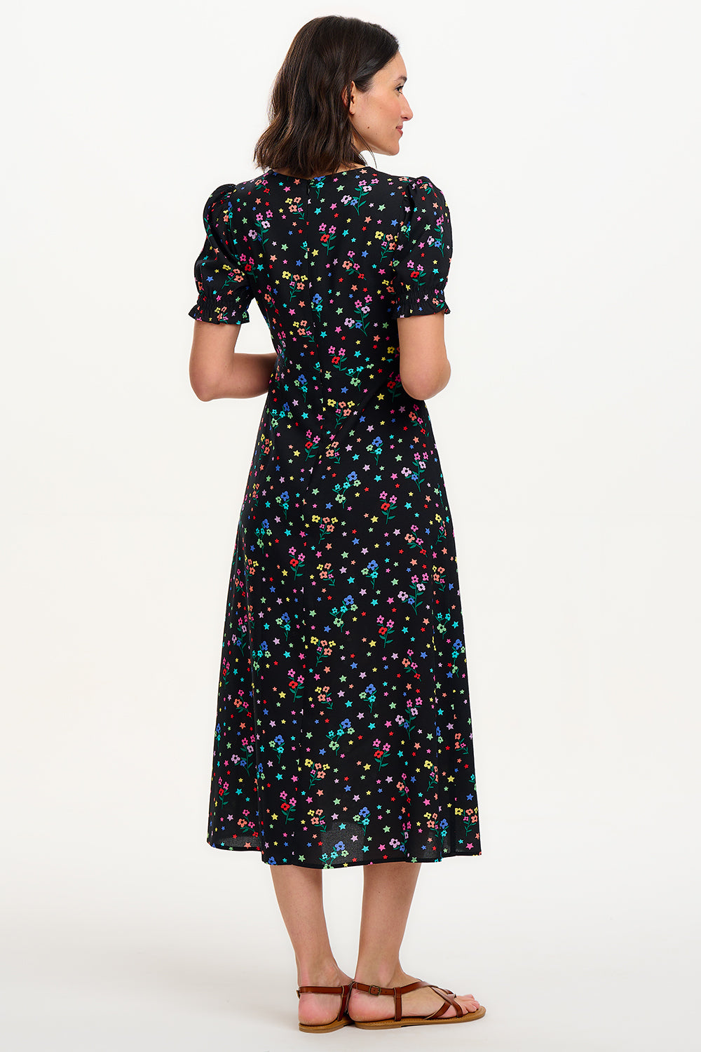 A model wearing a mid-length black dress with a V-neck and short-shirred sleeves, adorned with a multicolor floral and star print.