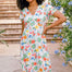A woman wearing an off-white midi dress with a tropical hummingbird print, featuring a V-neck and short-shirred cuffs.