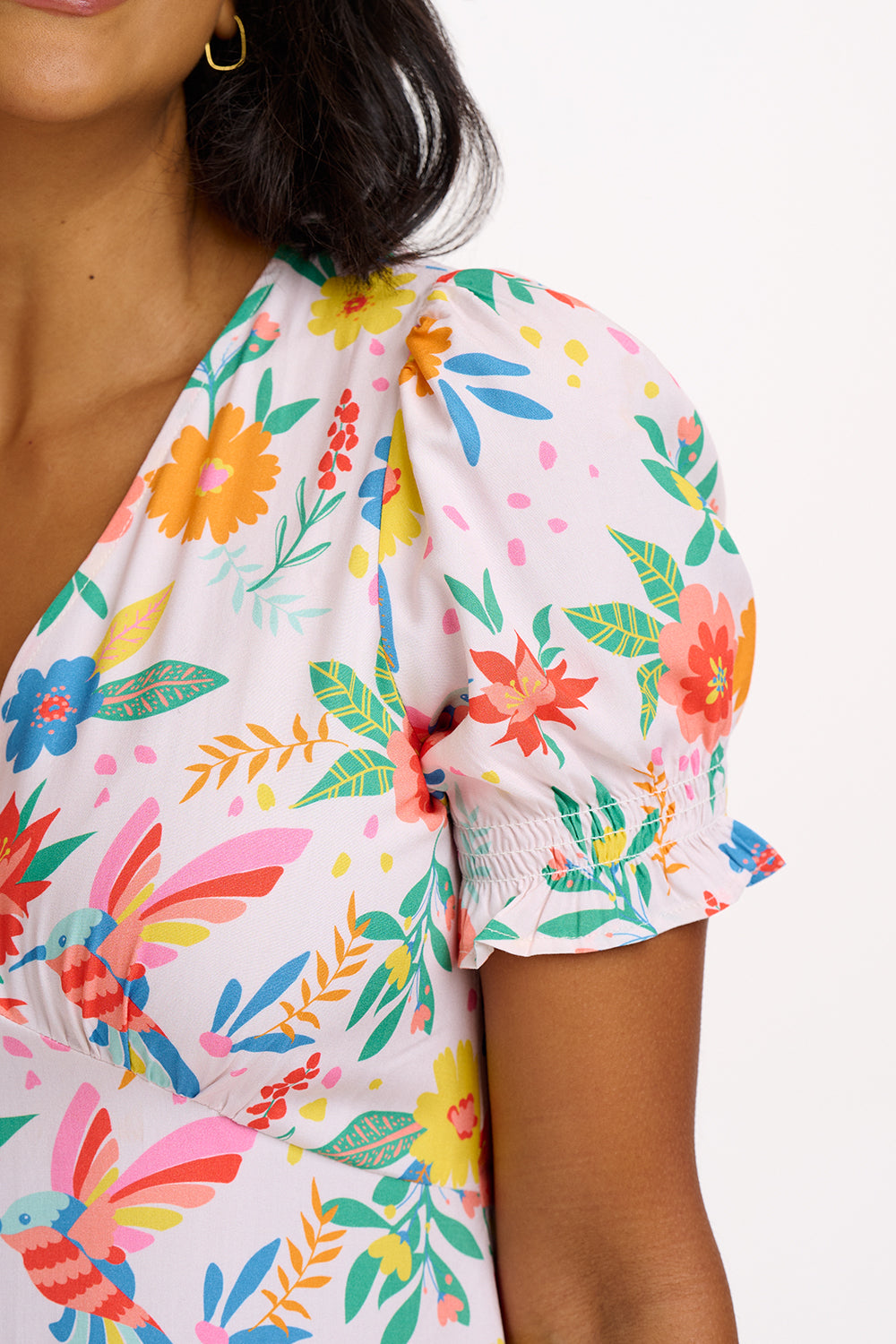 A model wearing an off-white midi dress with a tropical hummingbird print, featuring a V-neck and short shirred cuffs.