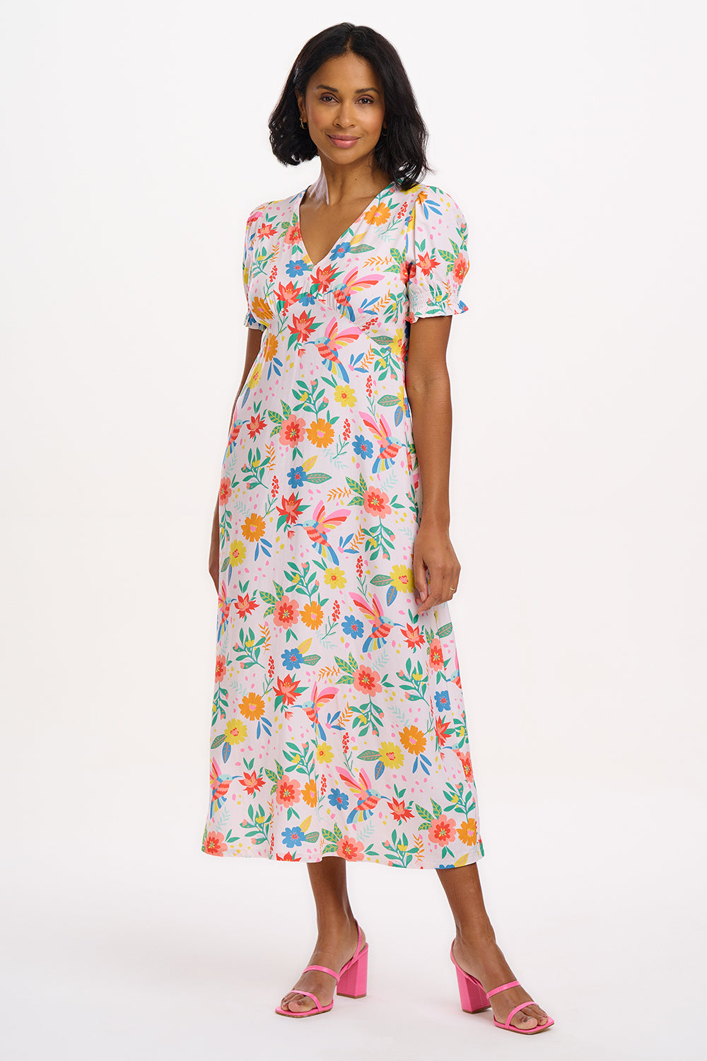 A model wearing an off-white midi dress with a tropical hummingbird print, featuring a V-neck and short shirred cuffs.
