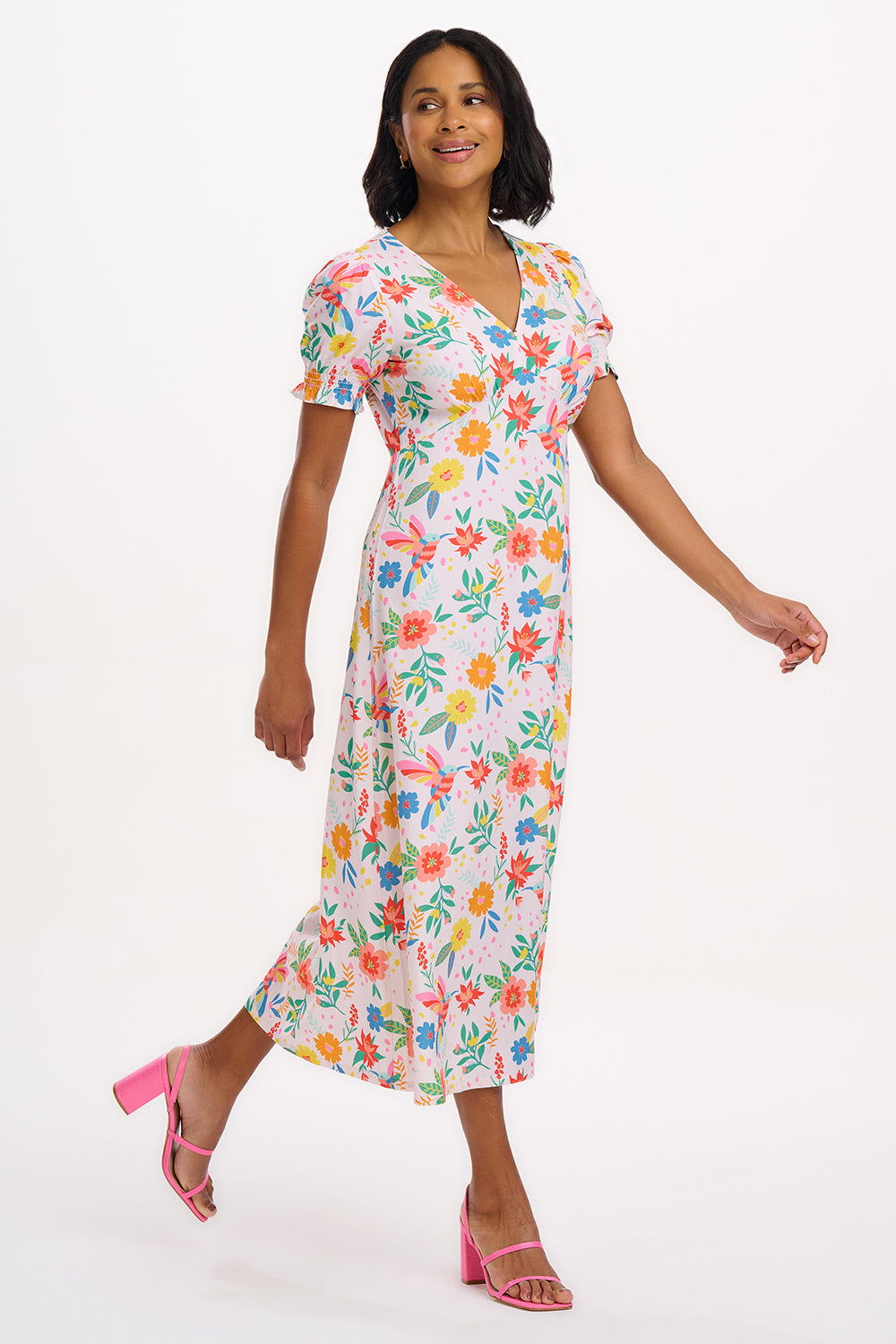 A model wearing an off-white midi dress with a tropical hummingbird print, featuring a V-neck and short shirred cuffs.