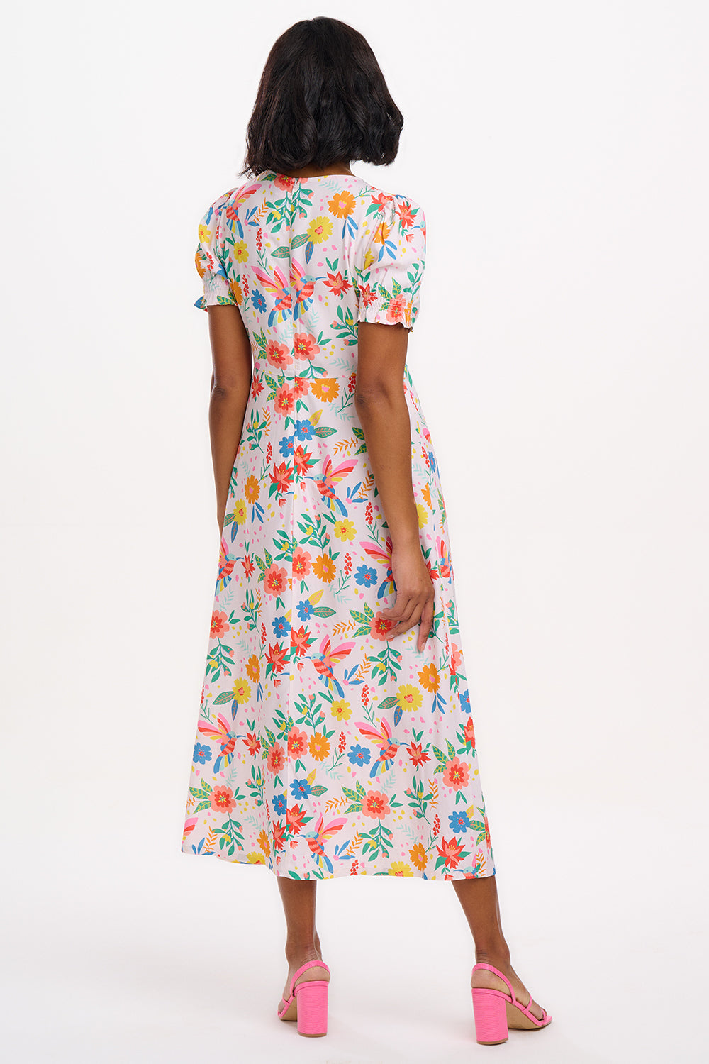 A model wearing an off-white midi dress with a tropical hummingbird print, featuring a V-neck and short shirred cuffs.