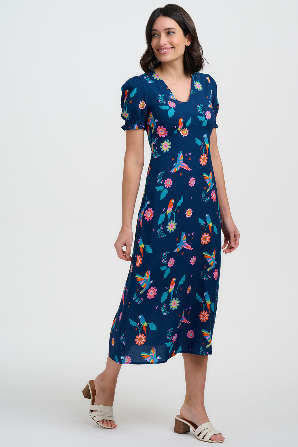 Woman wearing a navy dress with colorful floral and bird pattern on a white background