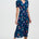 Woman wearing a navy dress with colorful floral and bird pattern on a white background