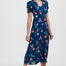 Woman wearing a navy dress with colorful floral and bird pattern on a white background